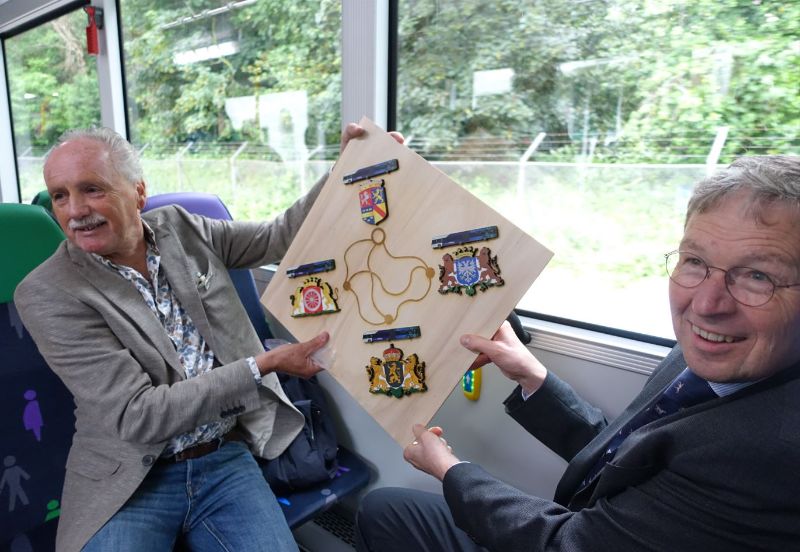 Der Projektmanager Trolley Infrastruktur Hans Aldenkamp überreicht dem Provinzialdirektor für Verkehr und Transport der Provinz Gelderland Klaas Ruitenberg die Wappen der Gemeinden, die der Trolleybus nun erschließt. Foto: J.Lehmann, 22.5.24